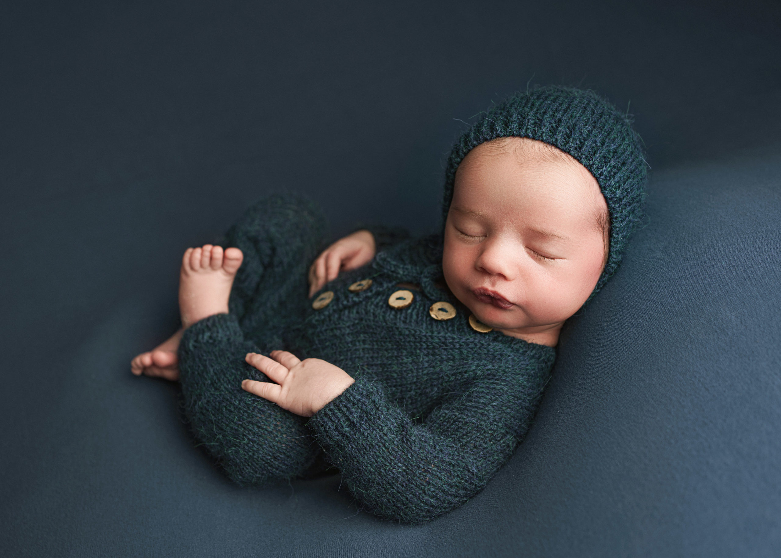 sleeping babyboy in a blue knit romper byMaddy-Rogers-Newborn-Training