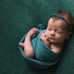 baby wrapped in a green wrap of fabric with headband