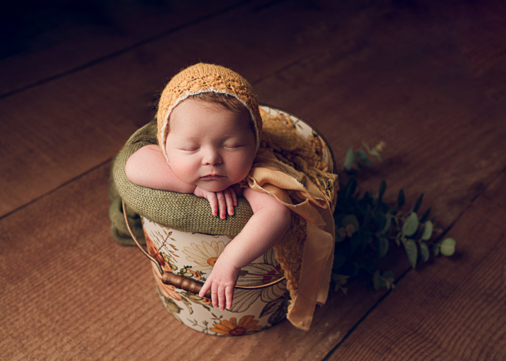 baby in a bucket with a yellow bonnet